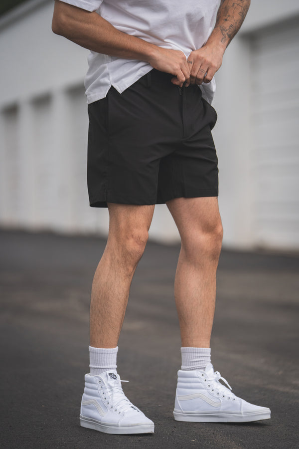 Man wearing a white t-shirt, black shorts, and white sneakers standing in front of a white building.