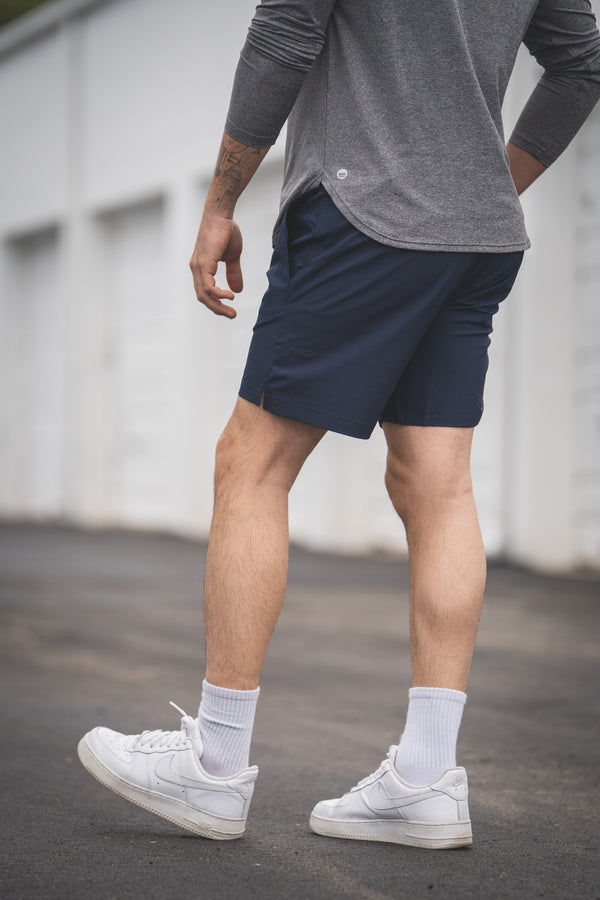 Person wearing navy shorts, gray shirt, white sneakers, and light gray socks on a blurred background