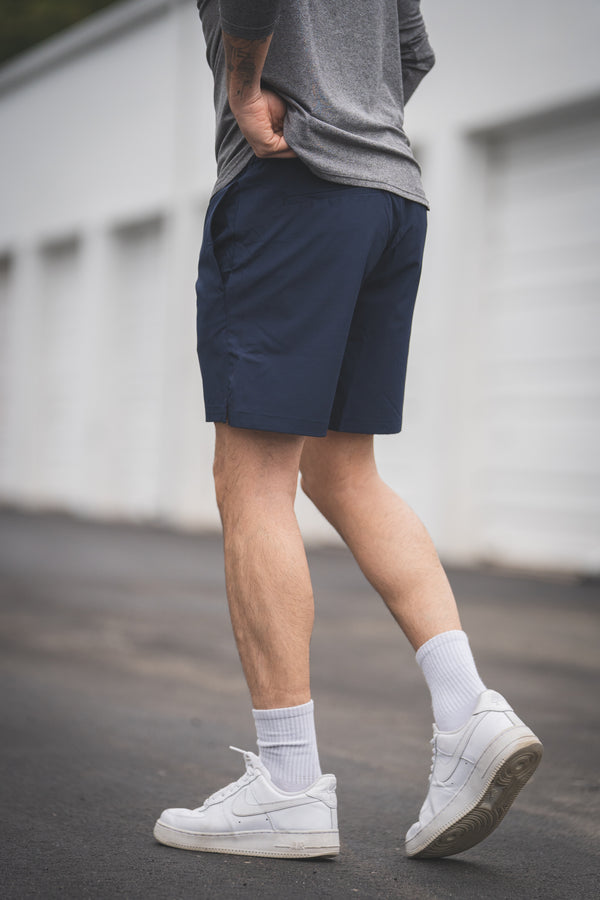 Person wearing navy shorts, gray shirt, white sneakers, and light socks on a blurred background